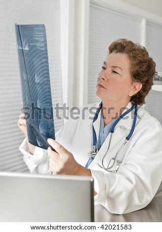 Mature female doctor or radiologist reading MRI film scan in a medical office setting.