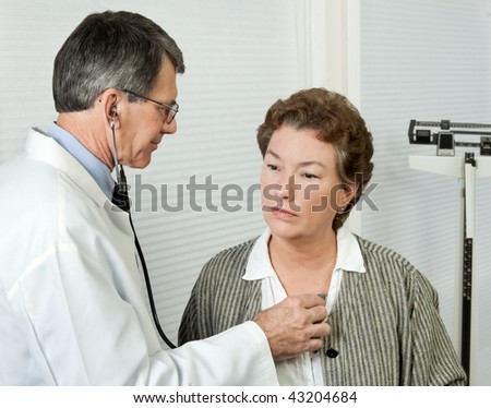 Male doctor listens to mature woman\'s heart during an office visit.