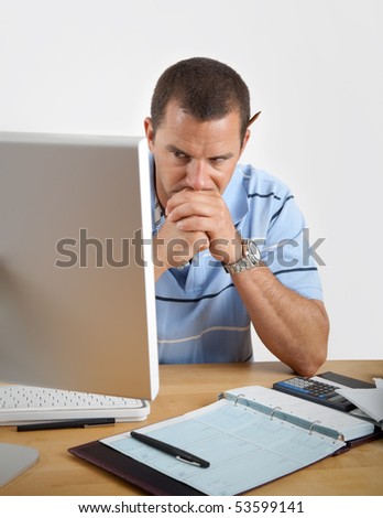 Young man looking tired, frustrated and worried as he sits at his desk with computer, checkbook and calculator.