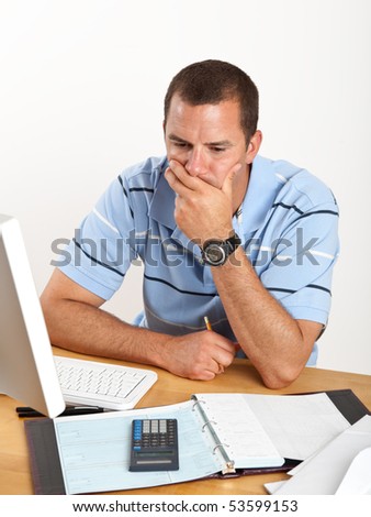 Worried young man, stressed out over bills and finances, sitting at desk with checkbook and computer.