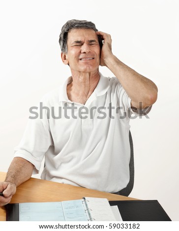 Mature man with headache at desk with checkbook, worrying about money and the economy.