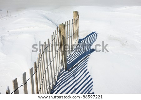 Simple landscape of sand fence and shadows on snowy white dunes at the beach. Sand fences play a vital part in conserving and growing sand dunes. Tiny bird tracks are evident to the left of the fence.