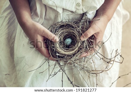 Vintage toned closeup of girl\'s hands holding a wild bird nest containing a blue and brown speckled egg. Soft romantic toning.