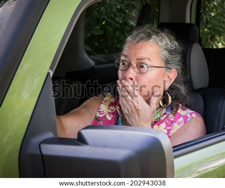 Sweaty, hot, senior woman driver looking terrified holding hand to mouth in driver\'s seat.