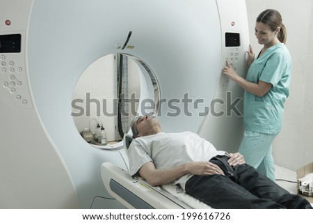 Young female doctor examining man in 40s with CT scanner. Computerised tomography.