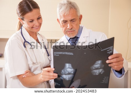 Senior male doctor analyzing mri scan with his smiling female assistant.