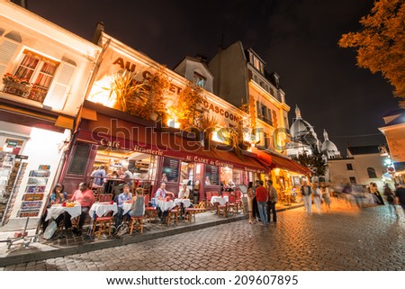 PARIS - JUNE 23, 2014: Tourists and locals walk in Montmartre streets at night. Montmartre attracted many famous modern painters in the early 20th century