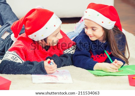 Happy brother and sister laying and writing with Christmas hat.