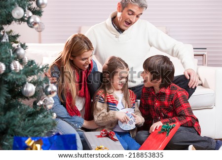 Happy family exchanging gifts under Christmas tree. Family and holiday concept. Parents and children.