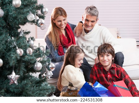 Happy family exchanging gifts under Christmas tree. Family and holiday concept. Parents and children.