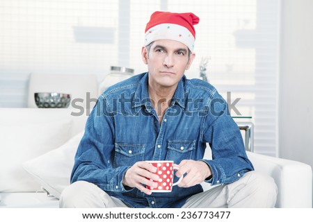 Thinking man with shirt, cup of coffee and Christmas hat at home.