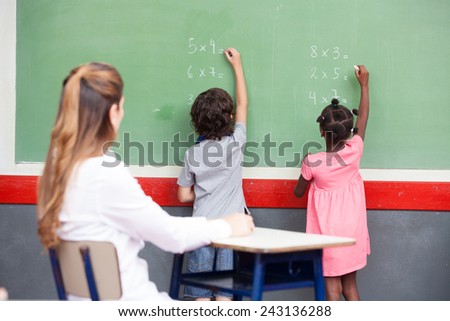 Learning mathematics at elementary school. Multi ethnic students writing on chalkboard with teacher observing.