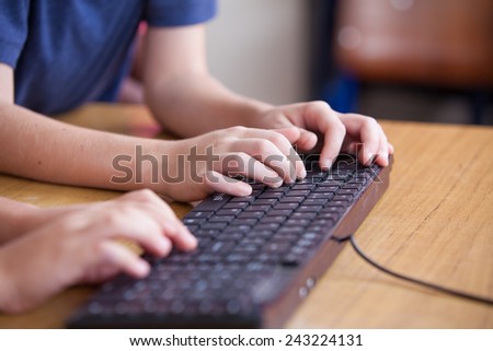 Students typing on computer keyboard at school.