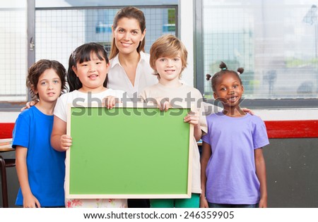 Happy multi-ethnic elementary classroom holding empty green chalkboard.
