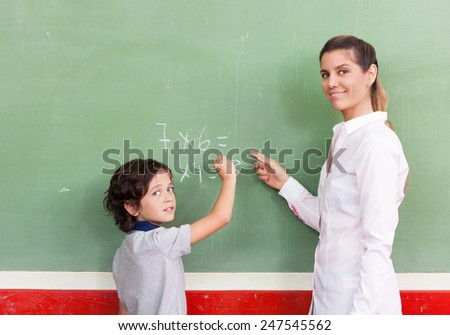 Female teacher with schoolboy at chalkboard.