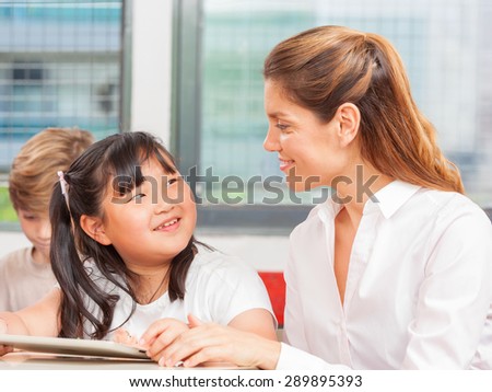 Teacher speaking to asian student while classmates writing on background.