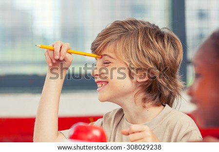 Happy young boy at school smiling holding pencil with right hand.