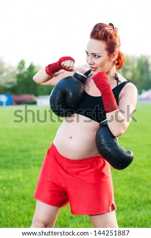 Pregnant young woman with boxing gloves on stadium
