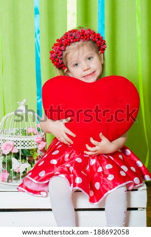 beautiful little girl in a red dress with a big red heart pillow