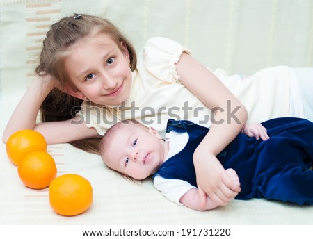 Older sister hugging baby lying on the bed with oranges