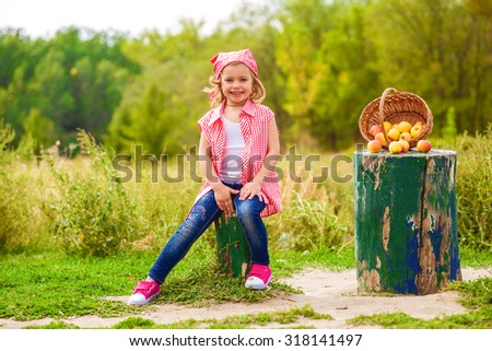 Little girl in jeans and a shirt near a river in autumn with apples