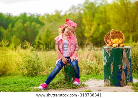 Little girl in jeans and a shirt near a river in autumn with apples
