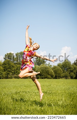 Pretty blonde young girl jumping in a park in a summer