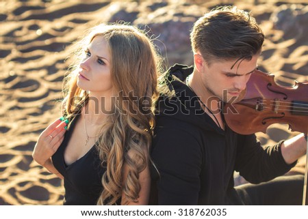 Beautiful couple violinist and young woman together over sand background