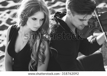 Beautiful couple violinist and young woman together over sand background. black and white