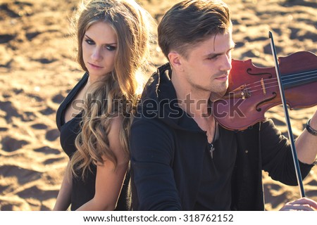 Beautiful couple violinist and young woman together over sand background