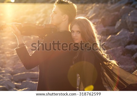 Beautiful couple violinist and young woman together over rocks and sand background