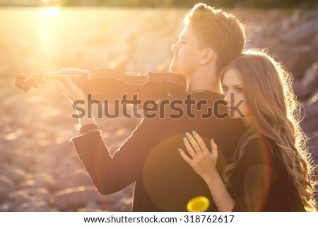 Beautiful couple violinist and young woman together over rocks and sand background