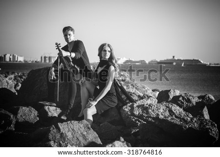 Beautiful couple violinist and young woman together near sea bay. black and white