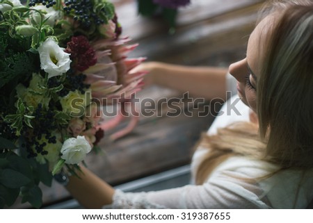 Florist at work: pretty young blond woman making fashion modern bouquet of different flowers