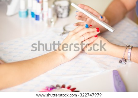 Closeup shot of a woman in a nail salon receiving a manicure by a beautician with nail file. Woman getting nail manicure. Beautician file nails to a customer.
