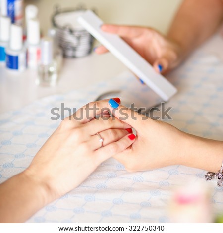 Closeup shot of a woman in a nail salon receiving a manicure by a \
\
beautician with nail file. Woman getting nail manicure. Beautician file \
\
nails to a customer.