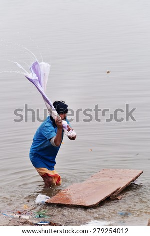 VARANASI, INDIA - DEC 23, 2014: Unidentified Indian man washes clothes in the holy water of the river Ganges in Varanasi. Uttar Pradesh, India
