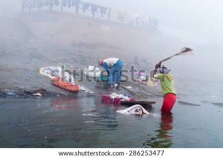 VARANASI, INDIA - DEC 24, 2014: Unidentified Indian man washes clothes in the holy water of the river Ganges at cold foggy winter morning. Varanasi. Uttar Pradesh, India