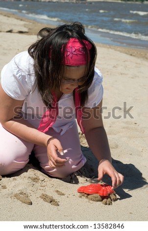 A young girl playing on the beach making sand sculptures