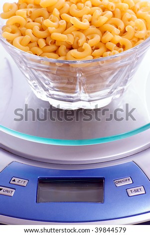 A bowl of uncooked macaroni full of carbohydrates, sitting on a food scale