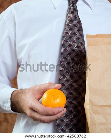 Closeup of a businessman holding his paper bagged lunch and an orange