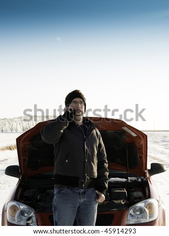 A young man is calling for help on his cell phone, while standing in front of a red car with it\'s hood up.  Copyspace is available on the top half of the image.
