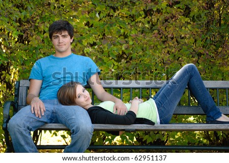 A young teenage girl is lying on a bench with her head on her boyfriend\'s lap.