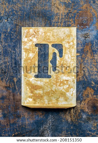 Metal typography over a weathered wood background showing the alphabet letter 