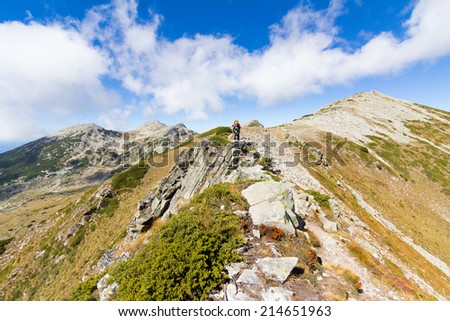 Woman mountaineer standing on mountain ridge and drinking water. Pirin national park, Bulgaria.