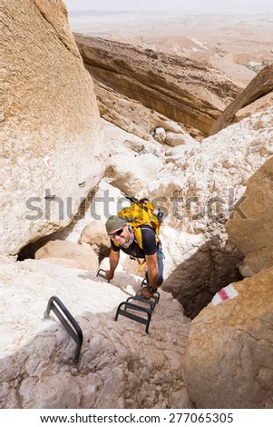 Man backpacker climbing rock canyon in Negev desert, Israel, on via ferrata iron steps.