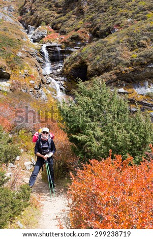 Young smiling happy woman backpacker mountaineer, standing mountain trail waterfall. Trekking Everest base Camp trail route, Nepal traveling, Himalaya tourism.