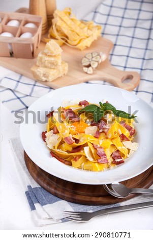 Pasta carbonara with tagliatelle spaghetti, egg yolk, bacon and basil. Rustic background with food and decorations. Top view on white background.