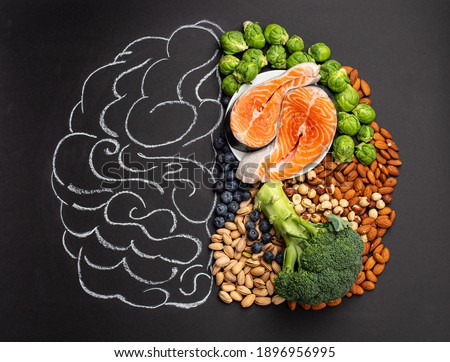Chalk hand drawn brain with assorted food, food for brain health and good memory: fresh salmon fish, green vegetables, nuts, berries on black background. Foods to boost brain power, top view