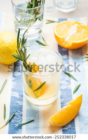 Orange rosemary fizz cocktail with ice and fresh herbs on a rustic fabric. Selective focus